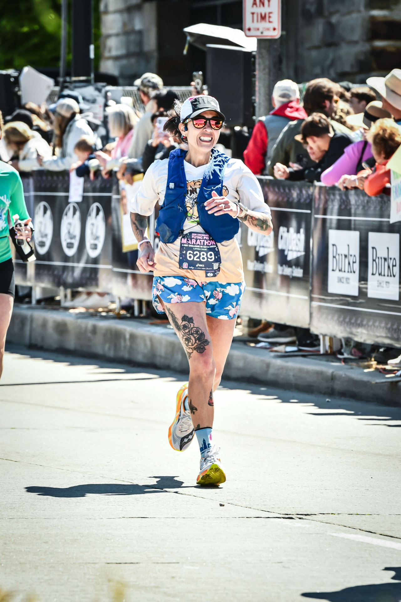 Dani smiling mid-race in a marathon, wearing a hydration vest and flying pig shorts.