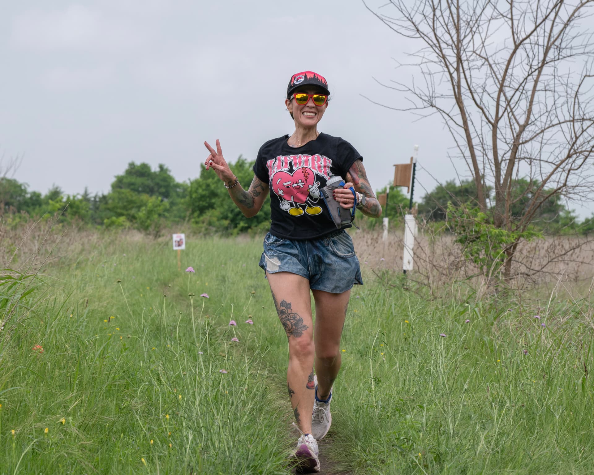 Dani trail running through tall grass, flashing a peace sign.