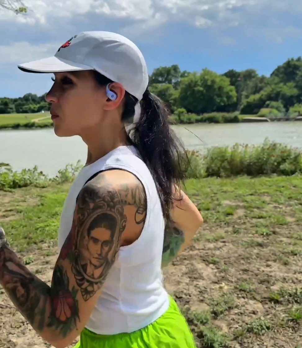 Dani running outdoors in a white cap wearing Raycon open-ear earbuds.