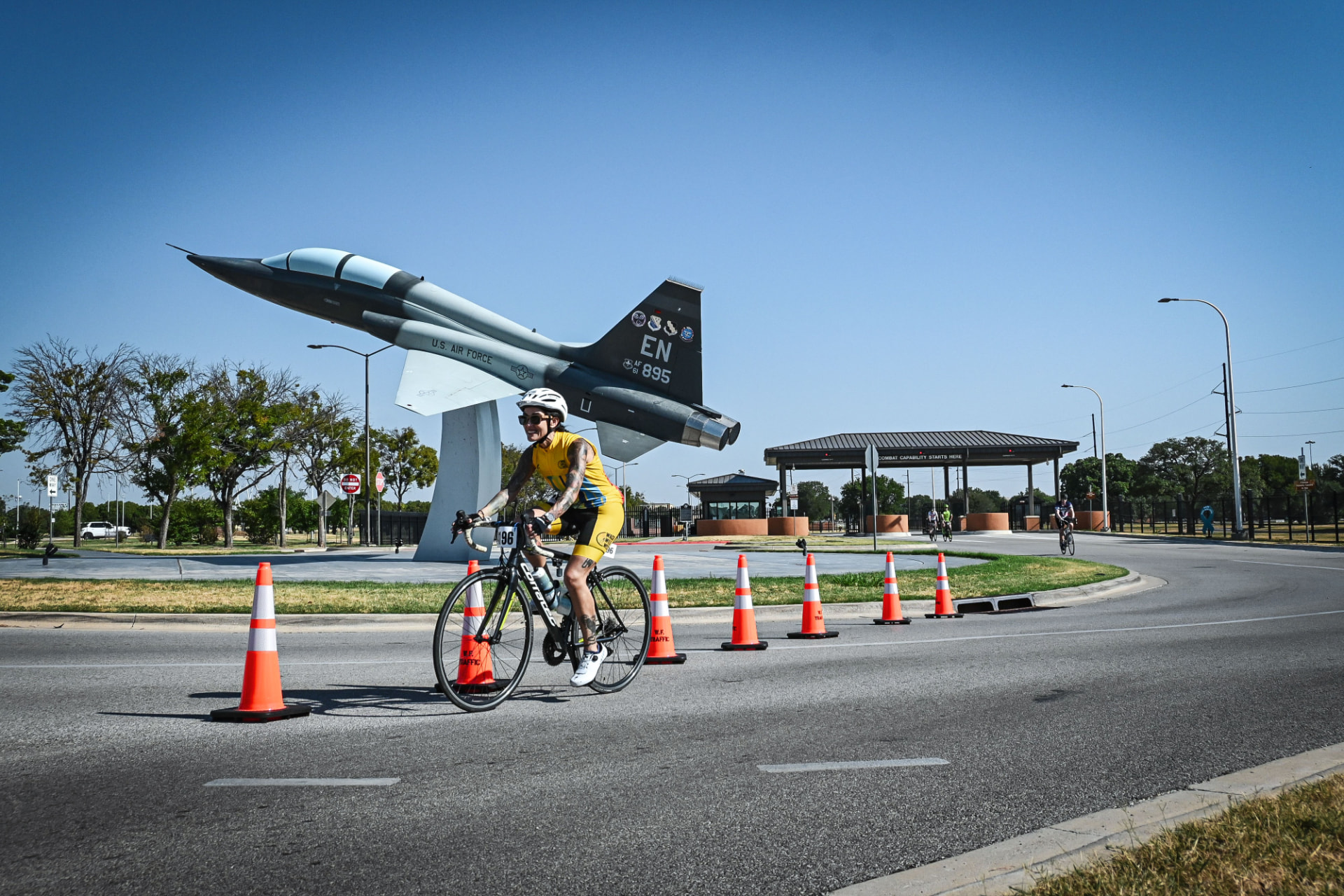 Dani cycling past a retired U.S. Air Force fighter jet on a sunny course.